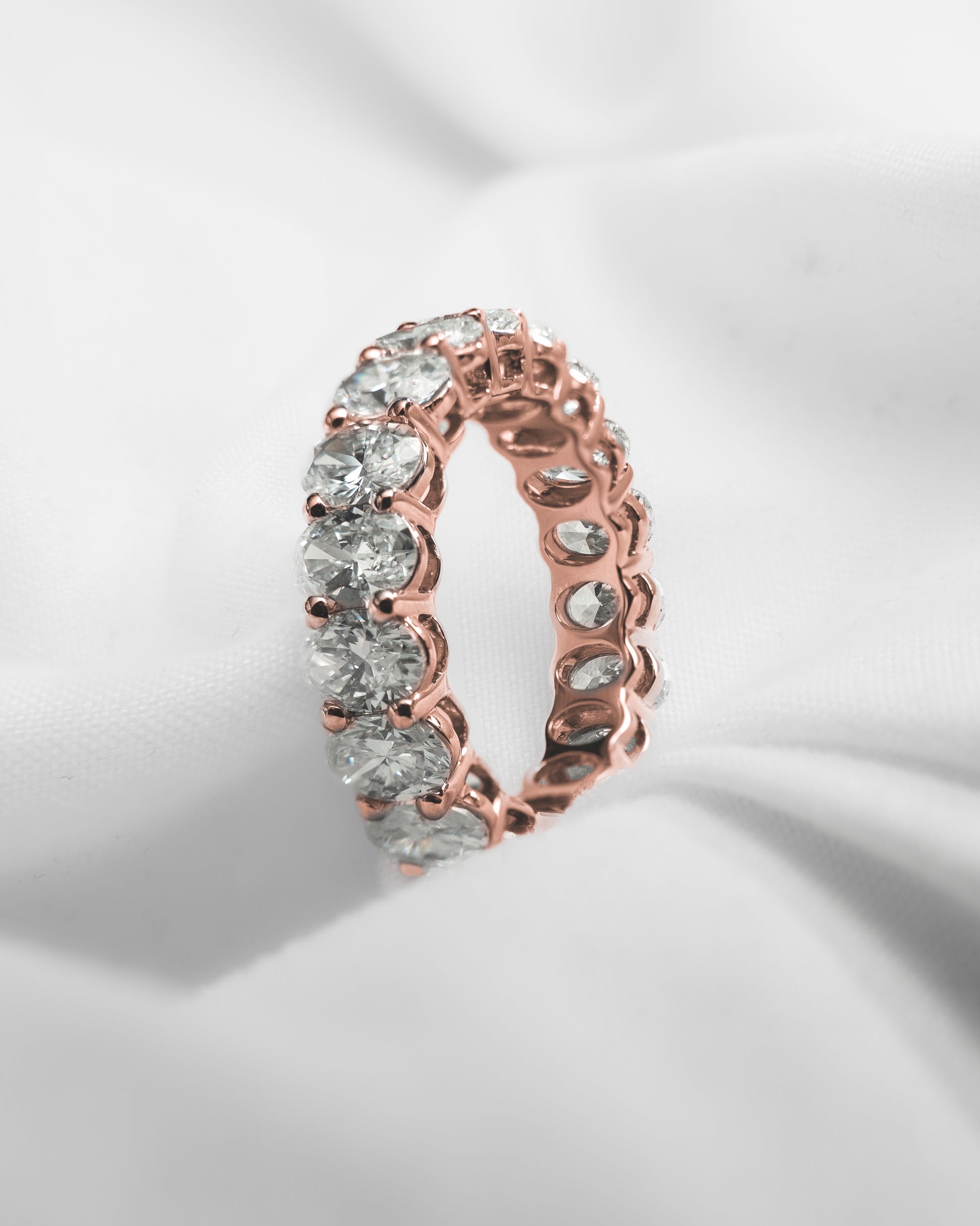 Rose gold ring with clear gemstones on a light gray background