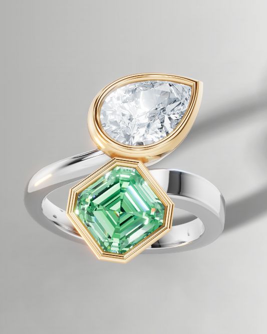 A silver and gold ring featuring a marquise-cut clear gemstone and a green emerald-cut gemstone, shown on a neutral gray background with a soft shadow.