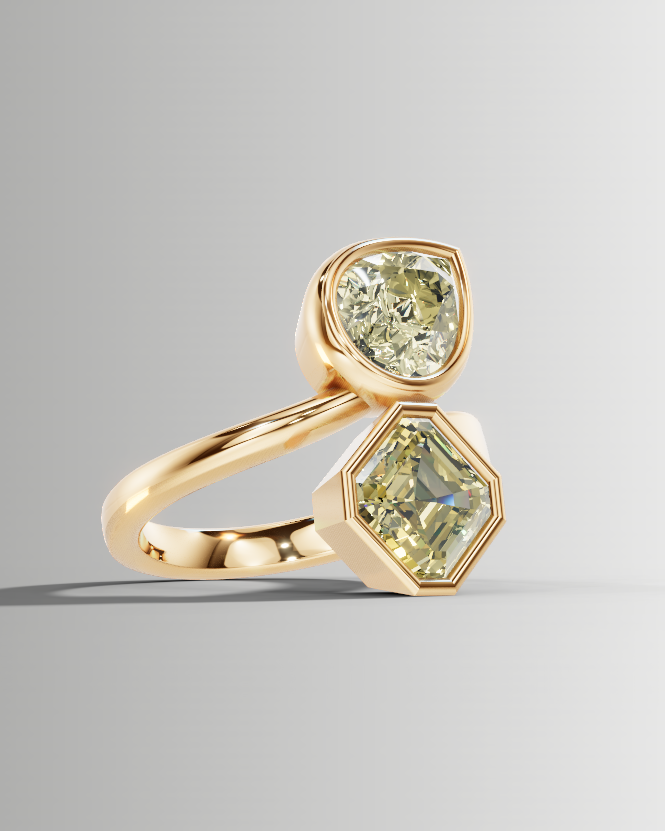 A gold ring featuring two light green gemstones, one round and one hexagonal, set on a smooth gray gradient background.