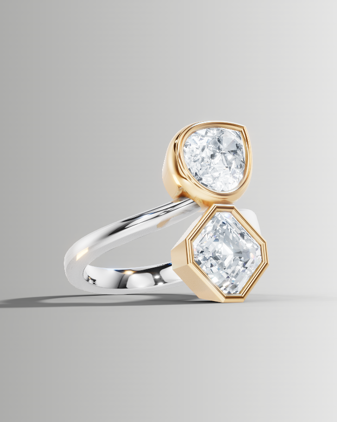 A unique ring featuring two clear gemstones in gold and silver settings, displayed on a neutral gray background.
