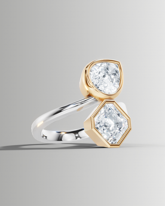 A unique ring featuring two clear gemstones in gold and silver settings, displayed on a neutral gray background.