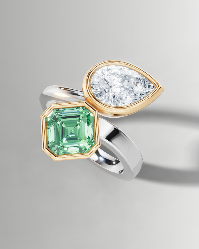 A two-stone ring featuring a square emerald-cut green gemstone in a gold setting and a pear-cut clear gemstone in a gold setting, mounted on a split silver and gold band, shown on a light gray background.