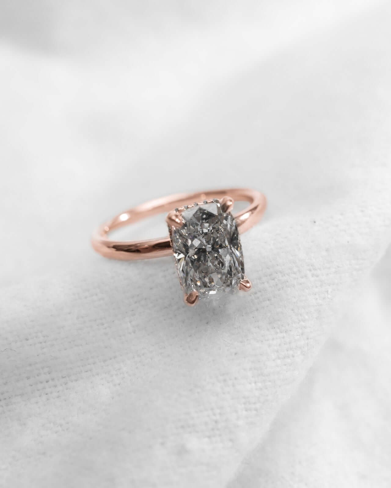 Elongated Cushion Lab Grown Diamond (Hidden Halo) | 18K Rose Gold engagement ring on soft fabric.