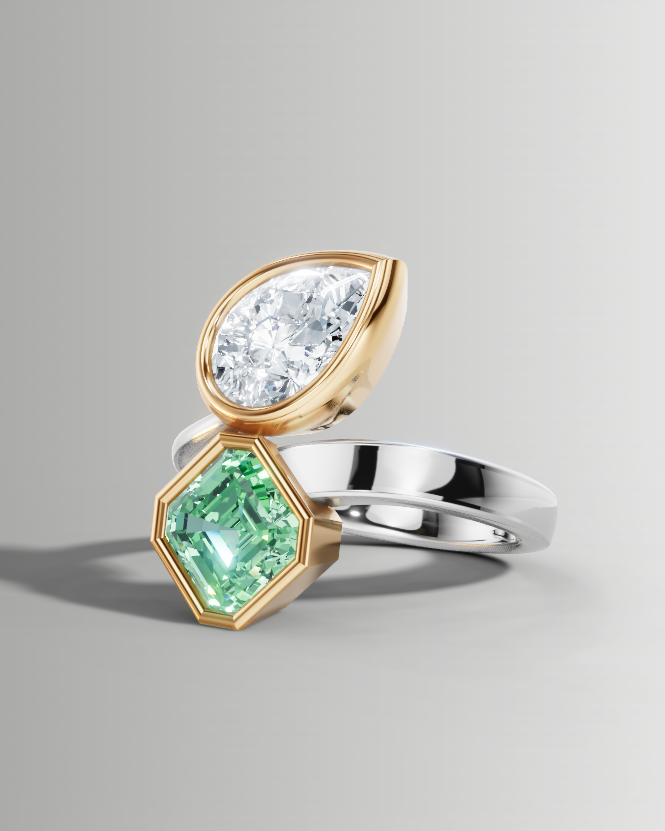A two-stone ring featuring a pear-cut clear gemstone in a gold setting and a hexagonal green gemstone in a yellow-gold setting, mounted on a silver-colored band, shown on a neutral gray background.